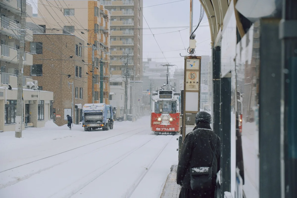 雪の降る札幌の街なか。線路の上を赤い市電が近づいてくる